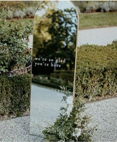 there is a large mirror on the ground in front of some bushes and trees with a message written on it