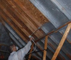 a man in white shirt and safety glasses working on an attic ceiling with wooden beams