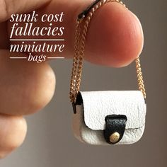 a miniature white and black purse on a gold filled chain is being held by a person's hand