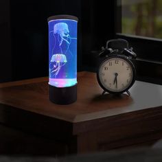 an alarm clock sitting on top of a wooden table next to a glass vase with jellyfish in it