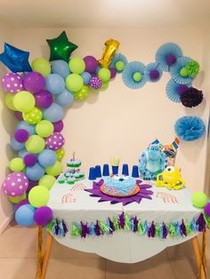 a birthday party with balloons and decorations on the wall behind a table that is decorated in blue, green, purple and yellow colors