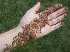 a person's hand with henna tattoos on it and grass in the background