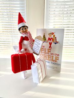 an elf is holding a gift and standing next to a book