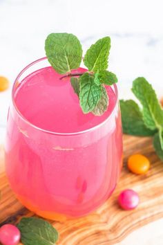 a pink drink in a glass with mint sprigs on the rim and candy candies around it