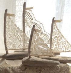 three wooden sailboats sitting on top of a table next to a lace covered curtain