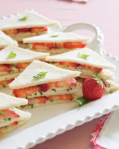 several sandwiches are arranged on a white platter with strawberries in the middle and mint sprigs