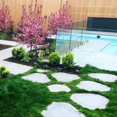 a small garden with stepping stones in the grass next to a swimming pool and wooden fence