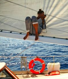 a woman sitting on the edge of a sailboat looking at the water while taking a photo