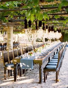 a long table with blue chairs and chandeliers hanging from the ceiling is surrounded by greenery