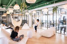 two women sitting on bean bag chairs in an office setting with hanging plants and suspended lights