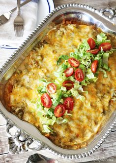 a casserole dish with tomatoes, lettuce and cheese in it on a silver platter