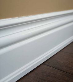 the edge of a white skirting board on a wood floor with a brown wall in the background