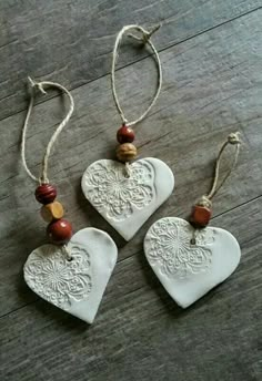 three ceramic heart ornaments hanging from strings on a wooden floor with beads and wood bead