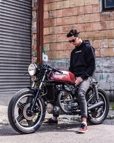 a man sitting on a motorcycle in front of a brick building with graffiti written on it