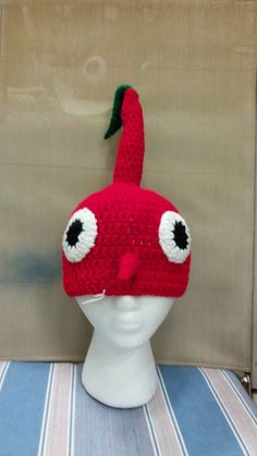 a crocheted red hat with eyes on top of a white head mannequin