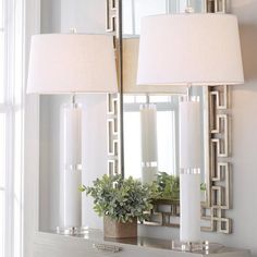 two lamps are sitting on top of a dresser in front of a mirror and plant