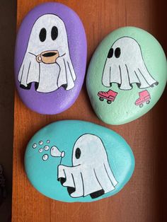 three painted rocks with ghost faces and skateboards on them, sitting on a table