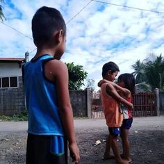 two young boys standing next to each other in front of a house with a blue sky and clouds behind them