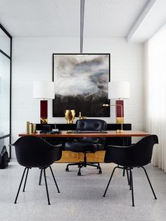 an office with black chairs and a large painting hanging on the wall above it's desk