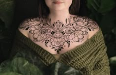 a woman with black and white tattoos on her chest is looking at the camera while surrounded by green leaves