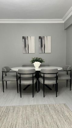 a dining room table with chairs and a vase on it's centerpiece in front of two paintings