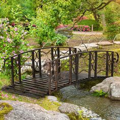 a small bridge over a stream in a park with rocks and flowers on the ground