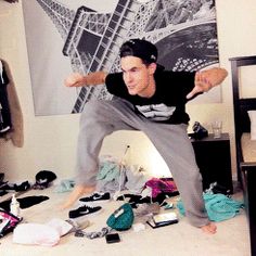 a man standing on top of a bed in a room filled with clothes and shoes