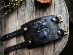 Hand tooled leather wristband with Wolf design.  This stylish  wristband features a unique design, with a hand-crafted wolf on the front.  Crafted from high-quality leather, this wristband is both durable and stylish.  The wolf muzzle is hand-carved and hand-painted onto the leather, ensuring that each  wristband is unique and one-of-a-kind. CUSTOM orders are always available. Simply send me a message regarding whatever personalization or change you would like to add to your order, and I will re Adjustable Black Hand Tooled Bracelet, Custom Handmade Leather Bracelets, Handmade Custom Leather Bracelet, Black Engraved Leather Bracelet, Handmade Black Leather Wristband, Adjustable Leather Bracelet, Leather Bracers, Black Leather Bracelet, Leather Wristbands