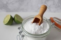 a jar filled with white powder next to two limes and a wooden scooper