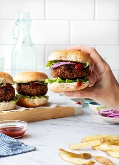 a person holding up a hamburger with lettuce and tomato