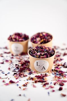 three small cups filled with flowers on top of a white table covered in confetti