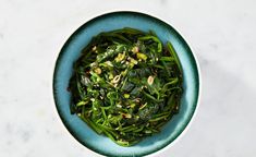 a blue bowl filled with green vegetables on top of a white table