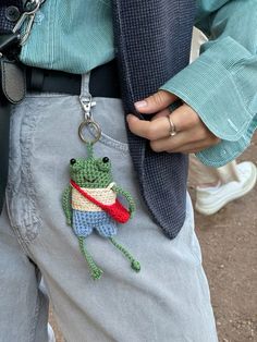 a person wearing a green frog keychain with a red cape on it's chest