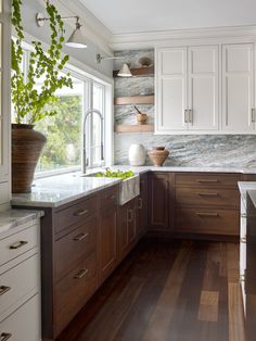 a kitchen with white cabinets and wooden floors, along with a large window that looks out onto the yard