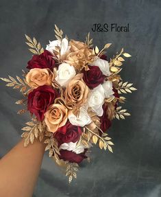 a bridal bouquet with red, white and gold flowers is held by someone's hand