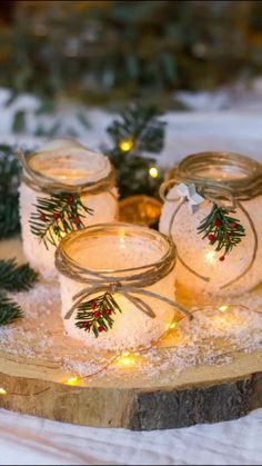 three mason jars with christmas lights are on a wooden board surrounded by evergreen branches and pine cones