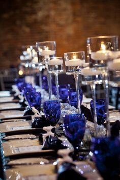 there are many candles on the table with purple and white flowers in them, as well as blue glassware