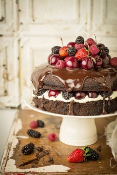 a cake with chocolate frosting and fresh berries on top is sitting on a table