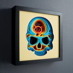 a framed art piece with a colorful skull on the wall next to a gray wall