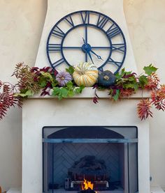 a fireplace with a clock on the mantle and fall foliage around it, as well as pumpkins