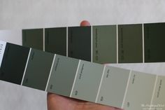 a hand holding two shades of gray and green paint swatches in their left hand