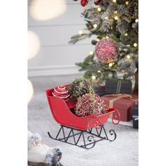 a red sleigh filled with christmas gifts next to a small christmas tree and presents