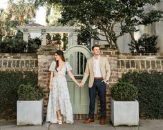 a man and woman holding hands standing in front of a gated entrance to a house