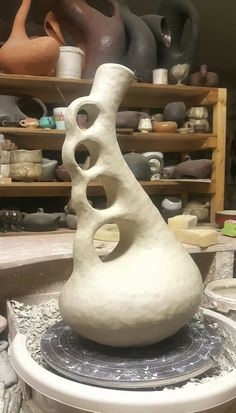 a large white vase sitting on top of a table next to shelves filled with pottery