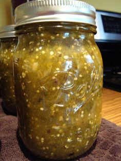 two jars filled with pickles sitting on top of a table next to a microwave