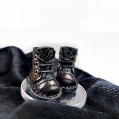 a pair of black baby shoes sitting on top of a white plate with black fabric