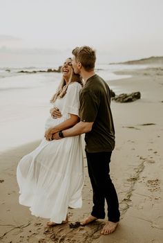 a man and woman standing on the beach with their arms around each other as they hug