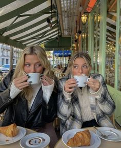 two women sitting at a table drinking coffee and croissants