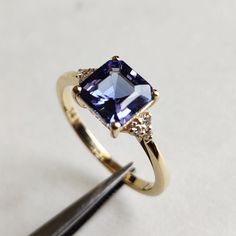 a gold ring with an amethyst blue stone surrounded by diamonds and a diamond tweezer