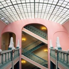 the inside of a pink building with stairs and railings on both sides, looking up at the skylight